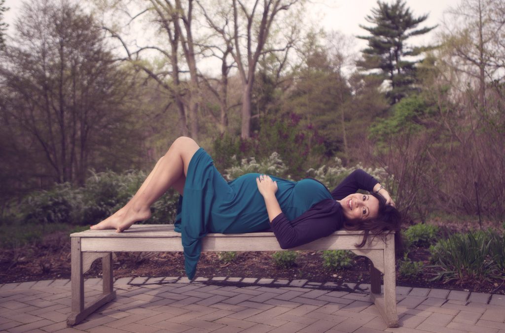 Photograph of a soon-to-be mom on a bench on location in a garden settin