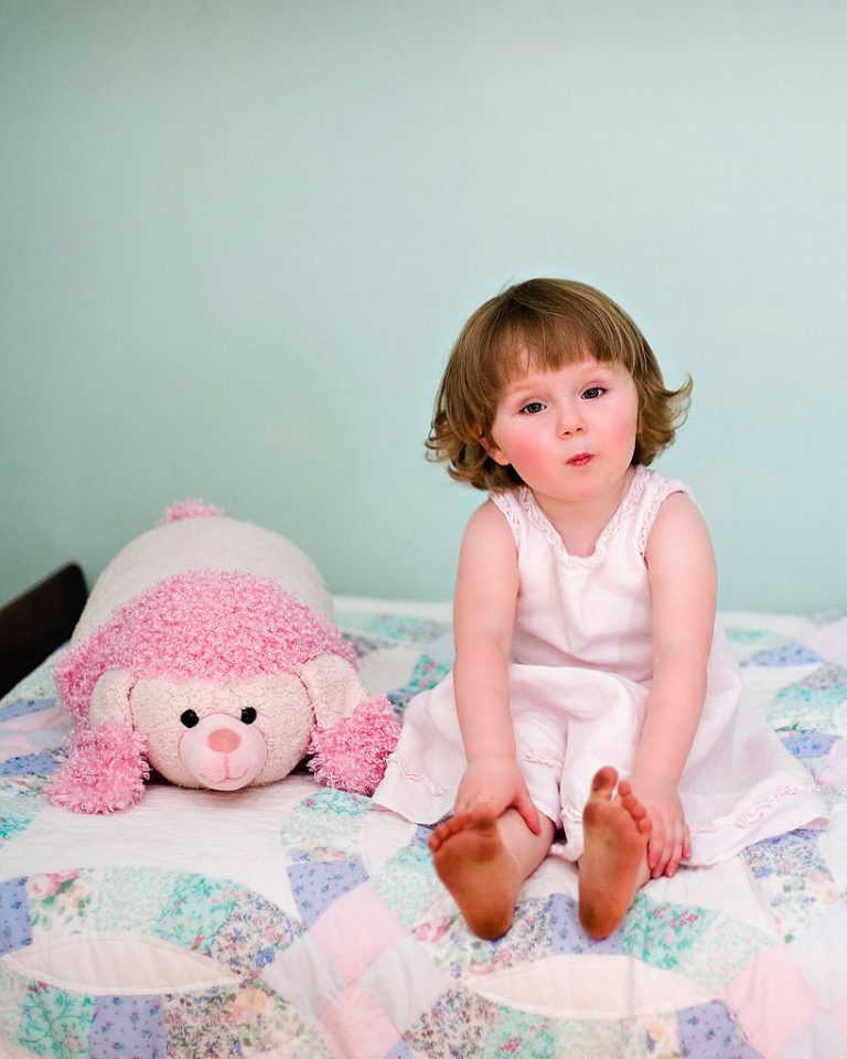 A cute toddler sits on her bed at home in Oak Park, photo on location by Marmalade Photography